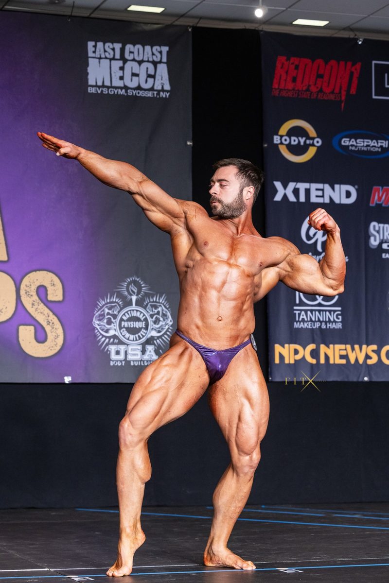 Derek Bolt on stage at an NPC bodybuilding show, side pose
